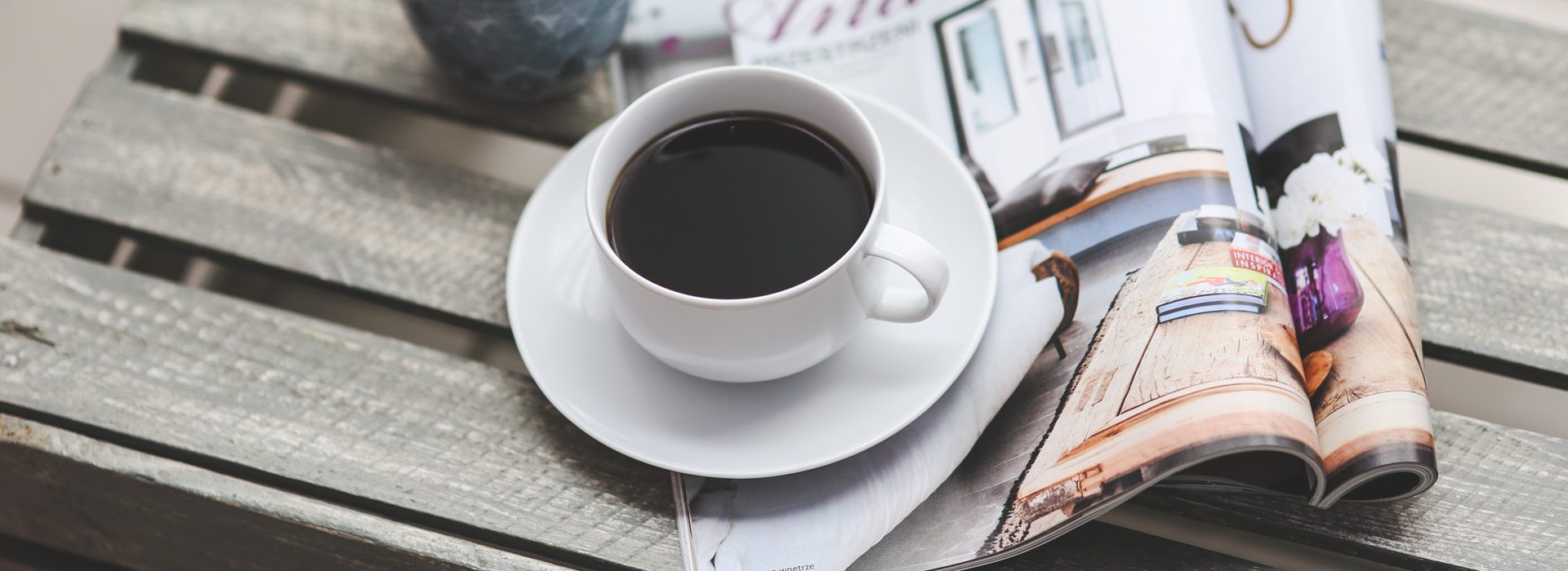 A képen egy magazin és egy csésze kávé látható egy asztalon.
